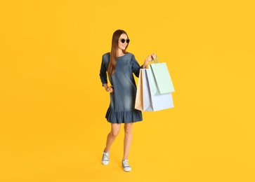 Beautiful young woman with paper shopping bags on yellow background Photo of Beautiful young woman with paper shopping bags on yellow background