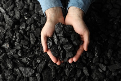Man holding coal in hands over pile, top view Photo of Man holding coal in hands over pile, top view