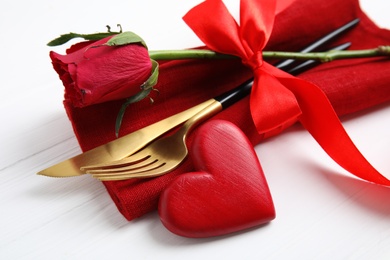 Closeup view of cutlery with napkin and decorative heart on white wooden table. Valentine's Day romantic dinner Photo of Closeup view of cutlery with napkin and decorative heart on white wooden table. Valentine's Day romantic dinner