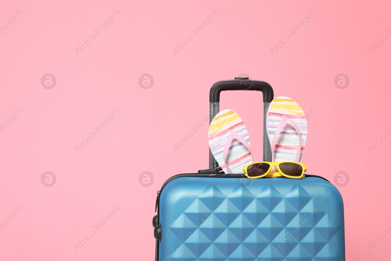 Stylish blue suitcase with flip flops and sunglasses on pink background. Space for text Photo of Stylish blue suitcase with flip flops and sunglasses on pink background. Space for text