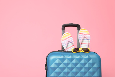 Photo of Stylish blue suitcase with flip flops and sunglasses on pink background. Space for text