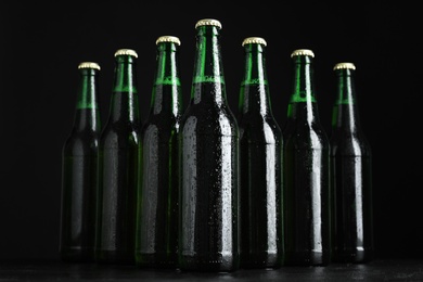 Glass bottles of beer on table against black background Photo of Glass bottles of beer on table against black background