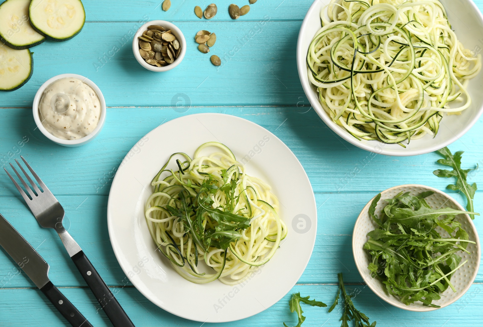Delicious zucchini pasta with arugula served on light blue wooden table, flat lay Photo of Delicious zucchini pasta with arugula served on light blue wooden table, flat lay