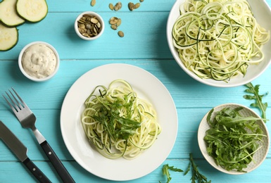 Delicious zucchini pasta with arugula served on light blue wooden table, flat lay Photo of Delicious zucchini pasta with arugula served on light blue wooden table, flat lay