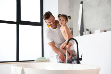 Photo of Young father with cute little daughter in bathroom