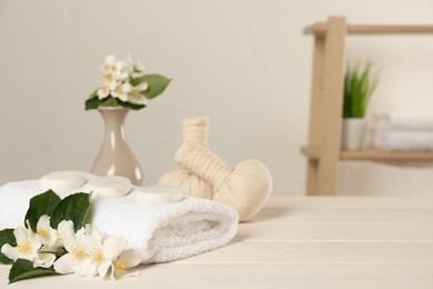 Beautiful jasmine flowers, towel, spa stones and herbal bags on white wooden table indoors, space for text Photo of Beautiful jasmine flowers, towel, spa stones and herbal bags on white wooden table indoors, space for text