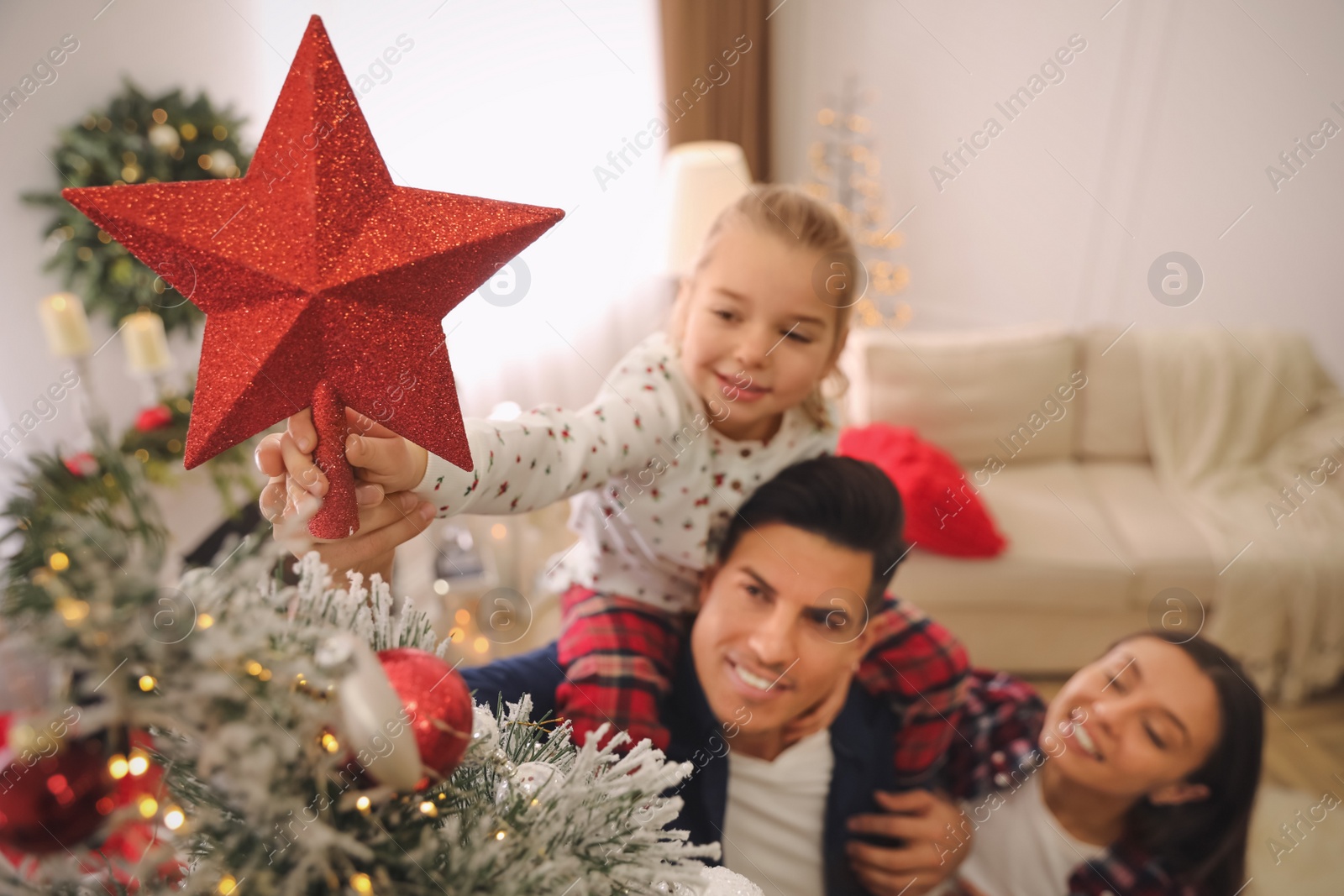 Family decorating Christmas tree indoors, focus on star topper Photo of Family decorating Christmas tree indoors, focus on star topper