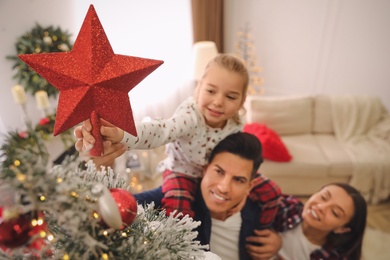 Family decorating Christmas tree indoors, focus on star topper Photo of Family decorating Christmas tree indoors, focus on star topper