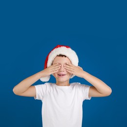 Happy little child in Santa hat closing eyes on blue background. Christmas celebration Image of Happy little child in Santa hat closing eyes on blue background. Christmas celebration