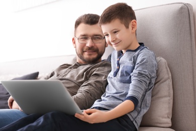 Photo of Little boy and his dad using laptop at home