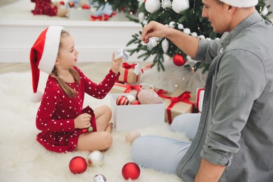 Father with his cute daughter decorating Christmas tree together at home Photo of Father with his cute daughter decorating Christmas tree together at home