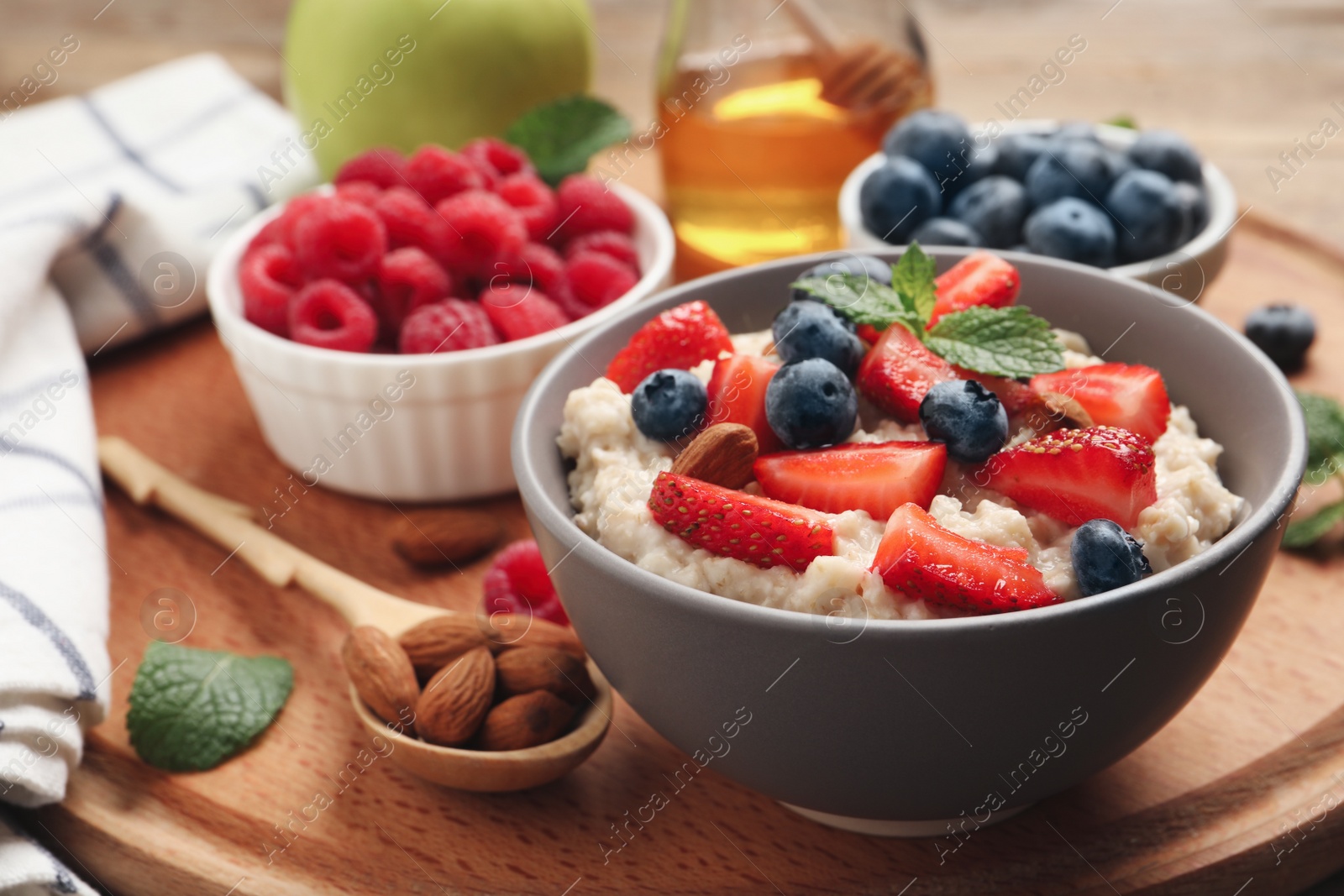 Tasty oatmeal porridge with berries and almond nuts in bowl served on wooden board Photo of Tasty oatmeal porridge with berries and almond nuts in bowl served on wooden board