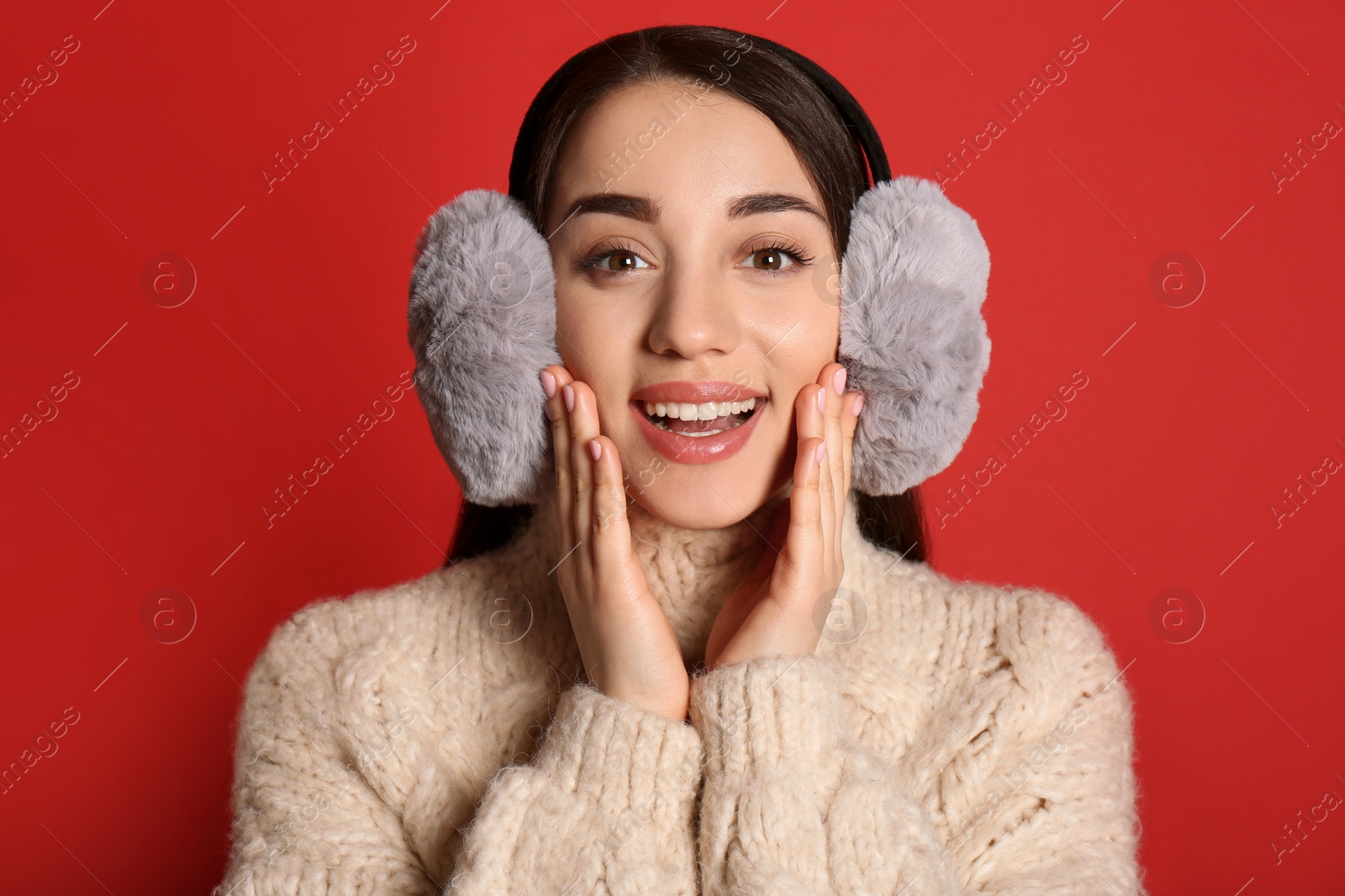 Beautiful young woman wearing earmuffs on red background Photo of Beautiful young woman wearing earmuffs on red background