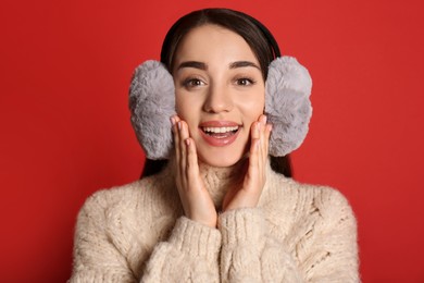 Beautiful young woman wearing earmuffs on red background Photo of Beautiful young woman wearing earmuffs on red background