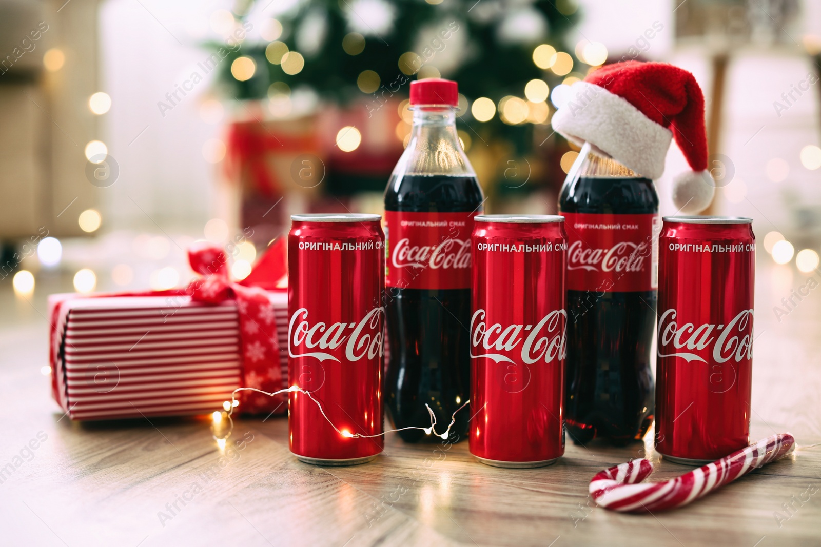MYKOLAIV, UKRAINE - January 01, 2021: Bottles and cans of Coca-Cola on floor against blurred Christmas lights Photo of MYKOLAIV, UKRAINE - January 01, 2021: Bottles and cans of Coca-Cola on floor against blurred Christmas lights