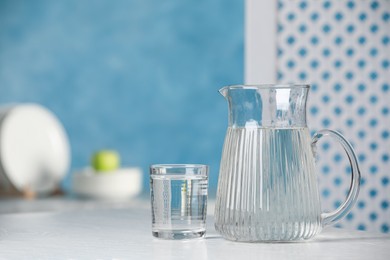 Jug and glass with water on white table indoors, space for text Photo of Jug and glass with water on white table indoors, space for text