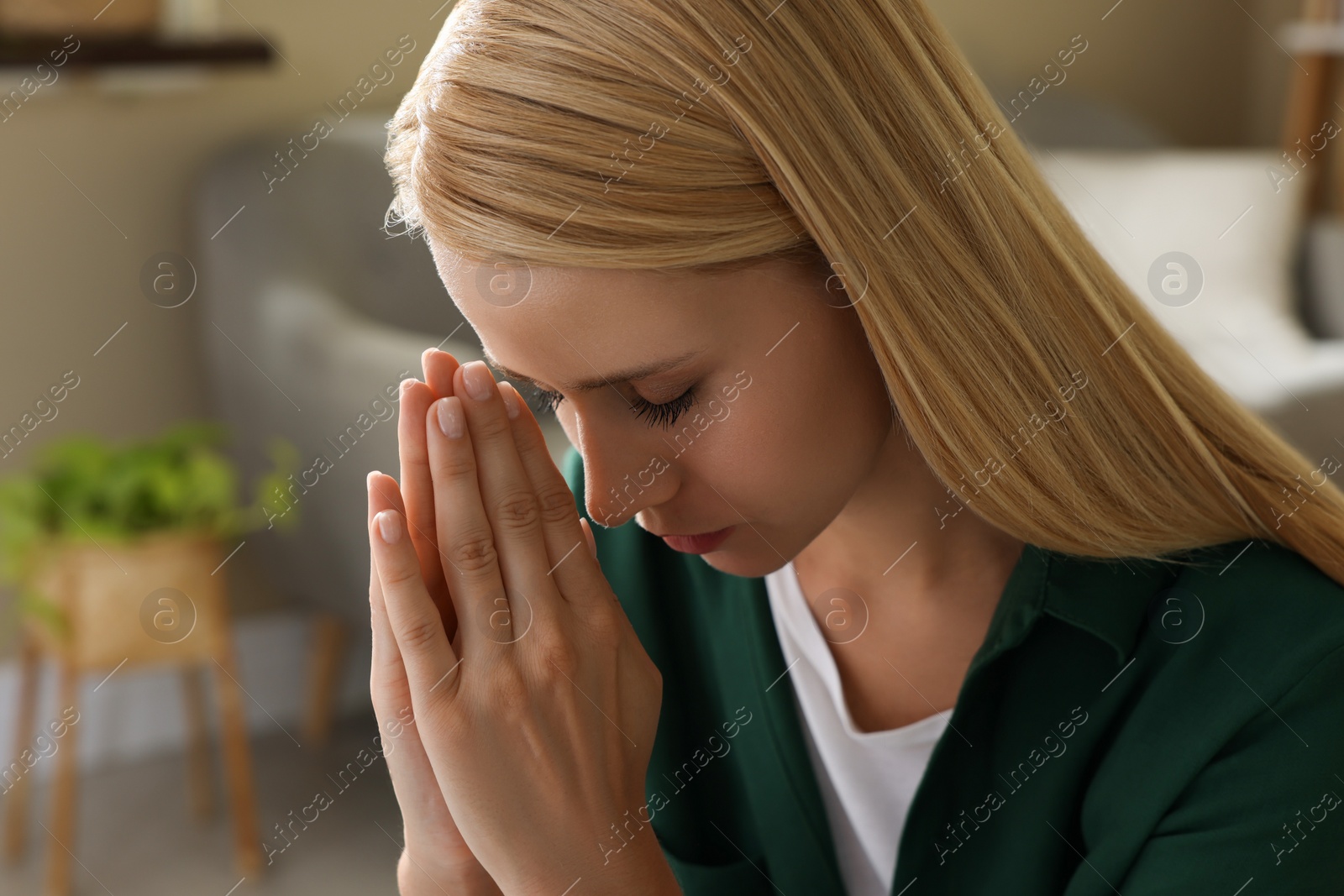 Religious young woman with clasped hands praying indoors Photo of Religious young woman with clasped hands praying indoors