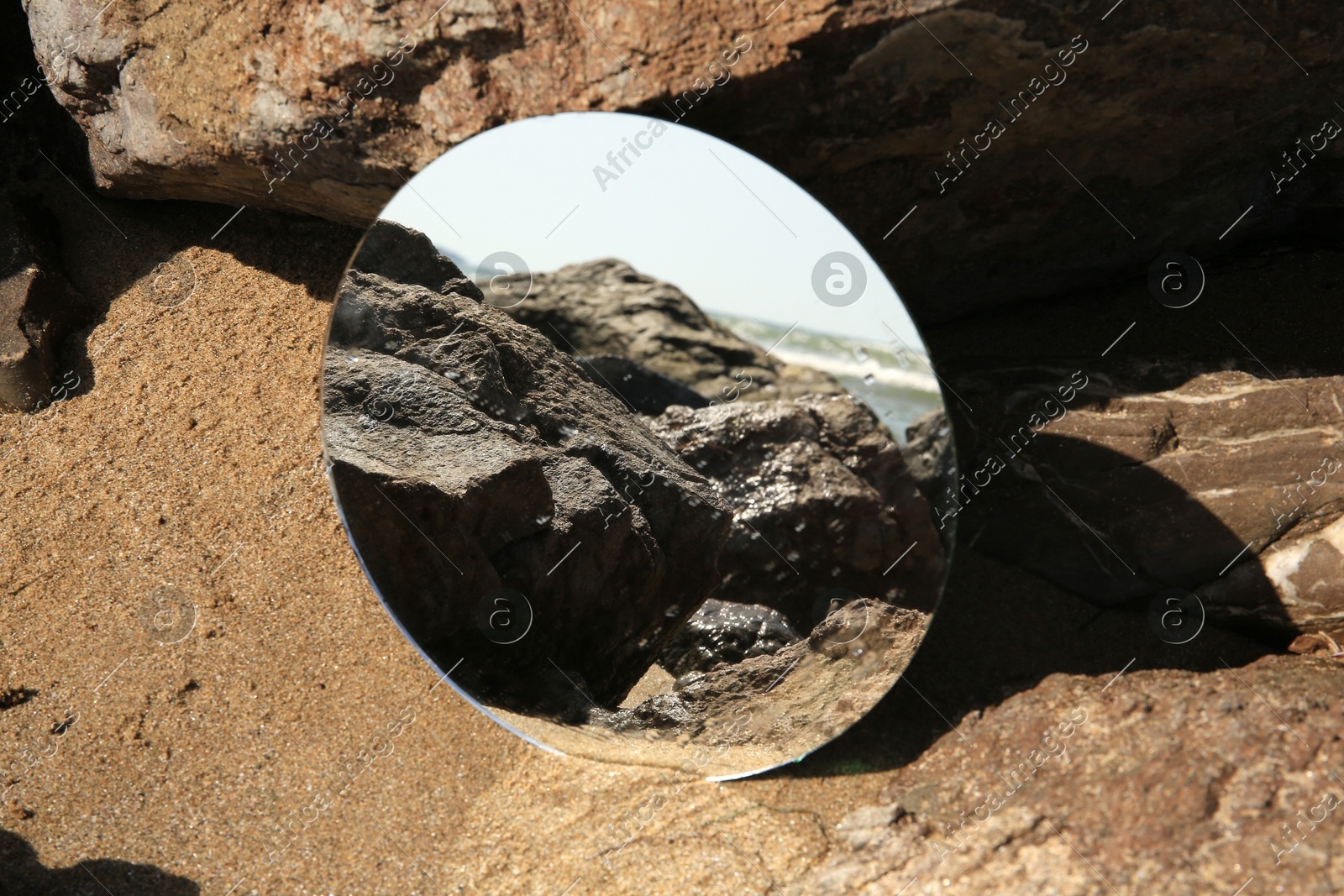 Round mirror reflecting beach on sand near stones outdoors Photo of Round mirror reflecting beach on sand near stones outdoors