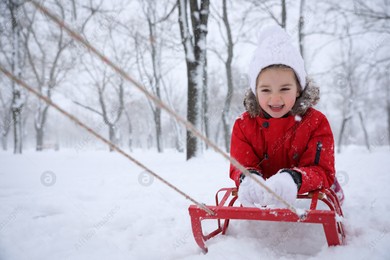 Cute little girl enjoying sleigh ride outdoors on winter day Photo of Cute little girl enjoying sleigh ride outdoors on winter day