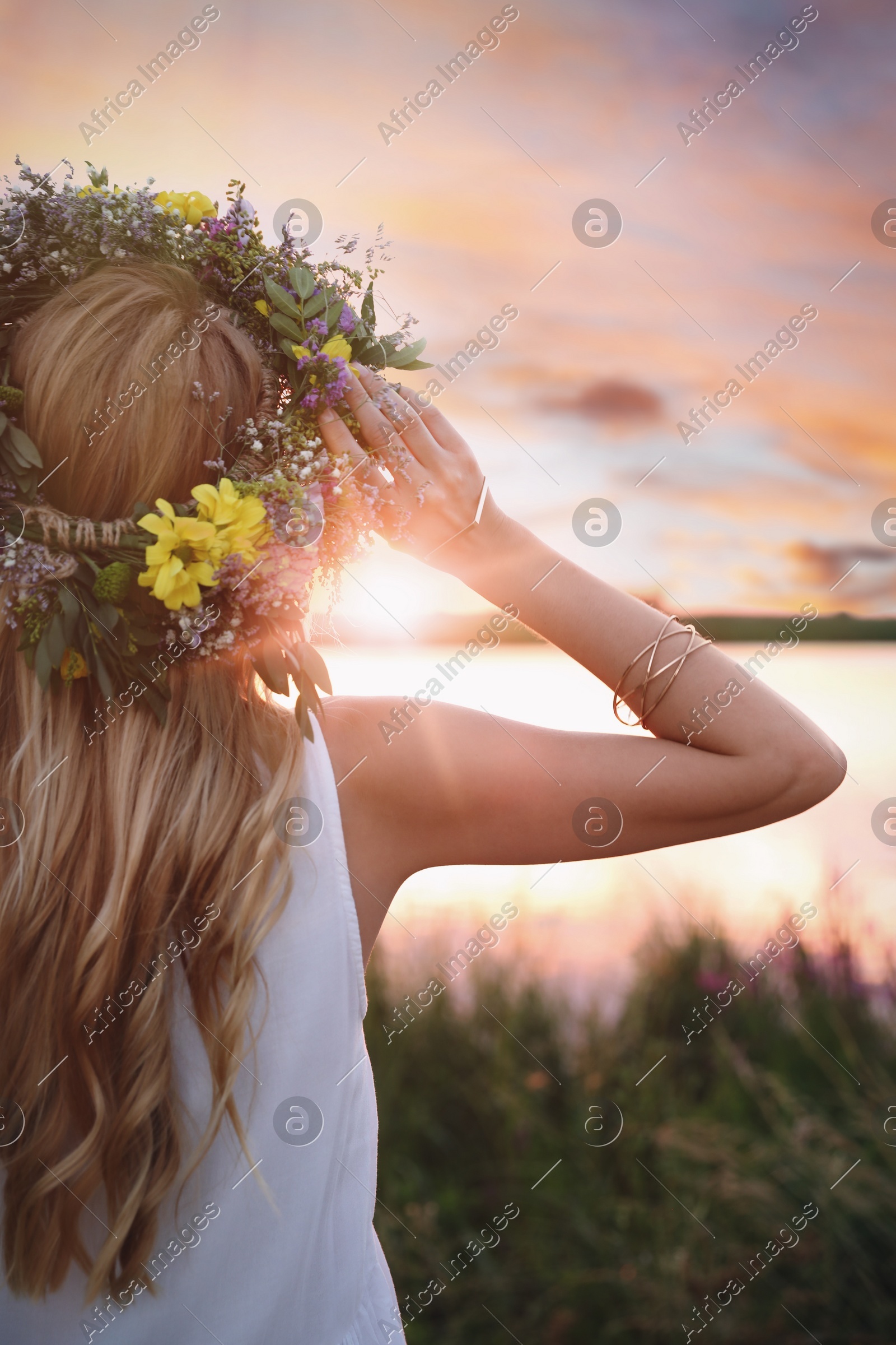 Young woman wearing wreath made of beautiful flowers outdoors at sunset Photo of Young woman wearing wreath made of beautiful flowers outdoors at sunset