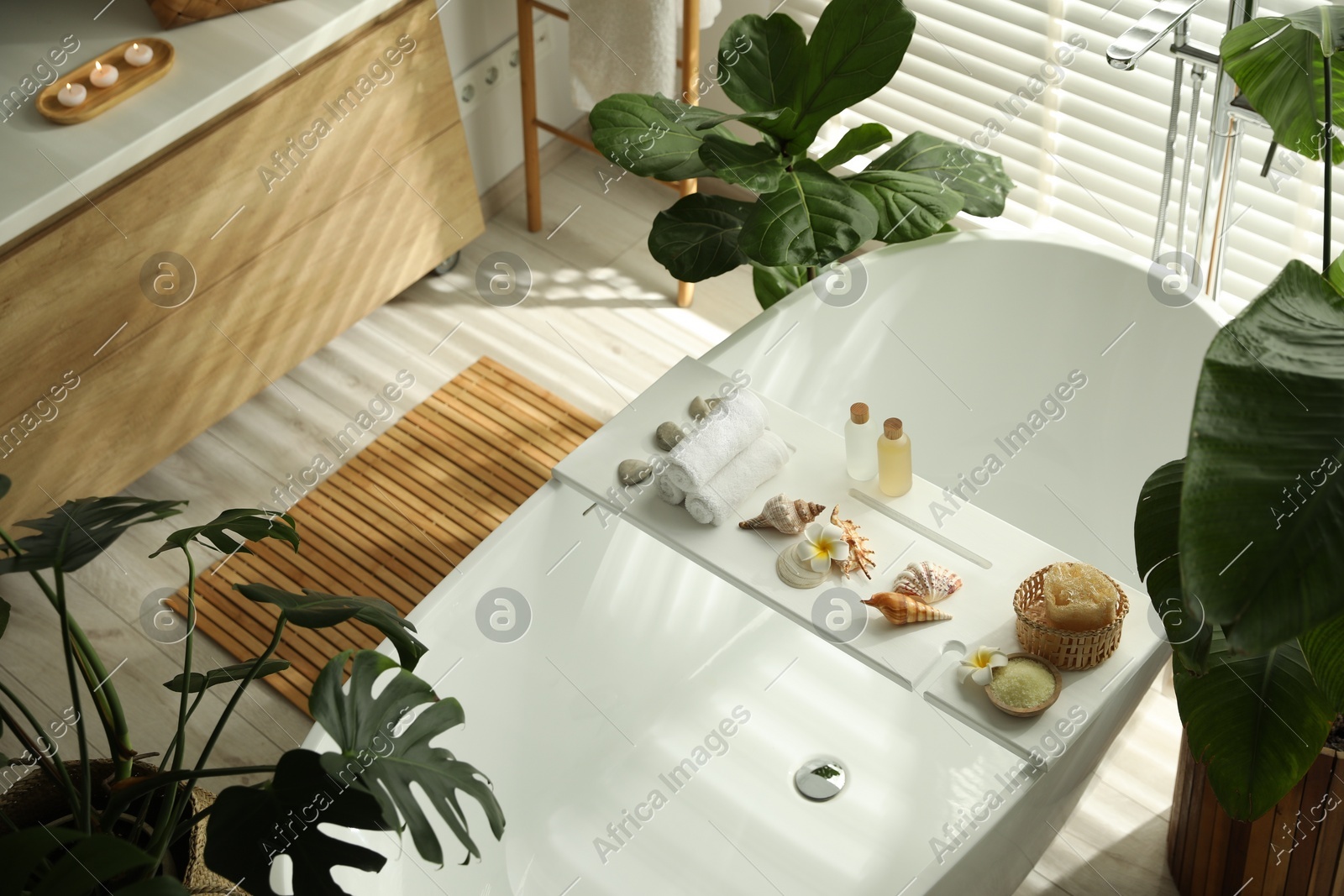 Bath tray with spa products, towels and shells on tub in bathroom, above view. Interior design Photo of Bath tray with spa products, towels and shells on tub in bathroom, above view. Interior design