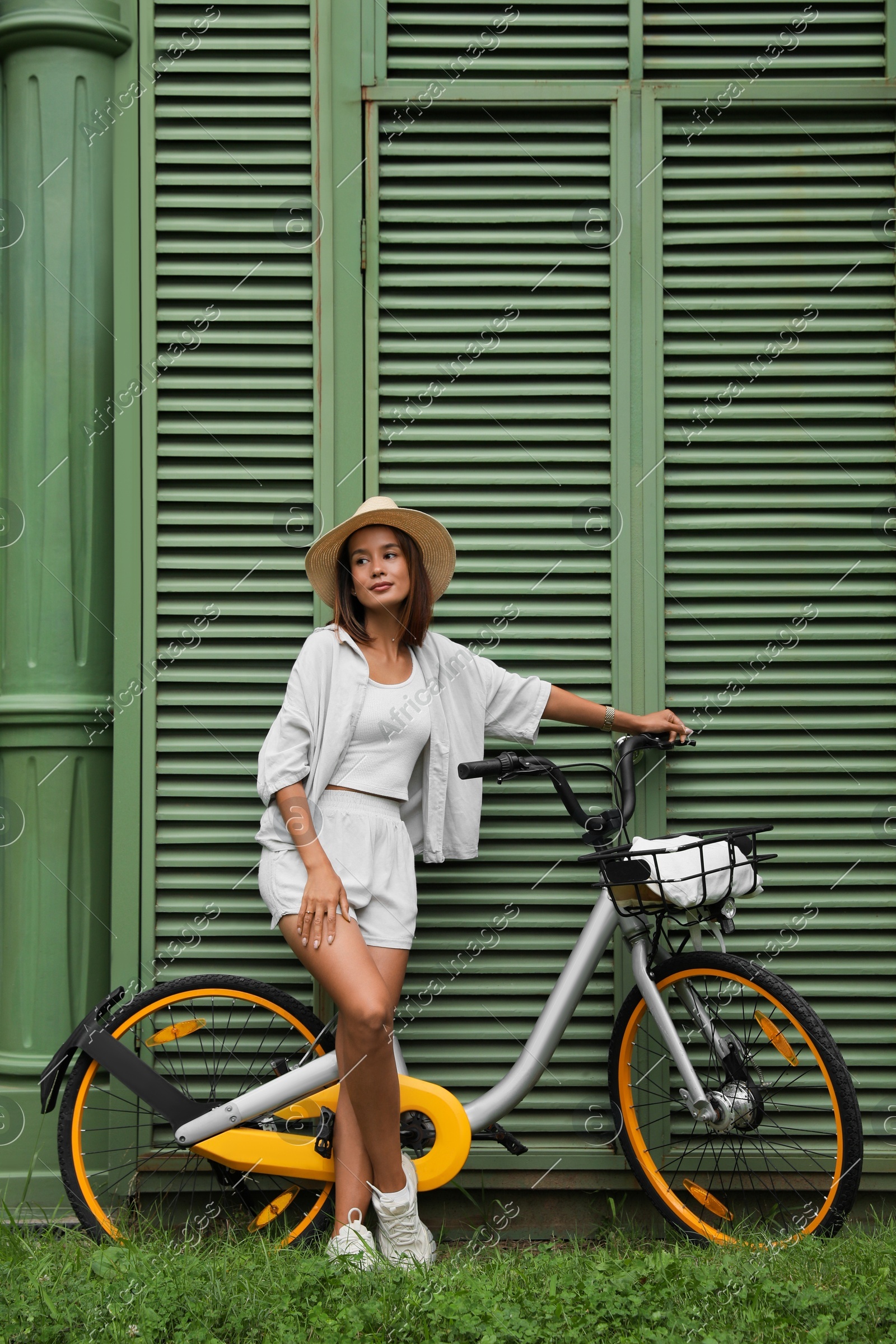 Beautiful young woman with bicycle near green wall outdoors Photo of Beautiful young woman with bicycle near green wall outdoors
