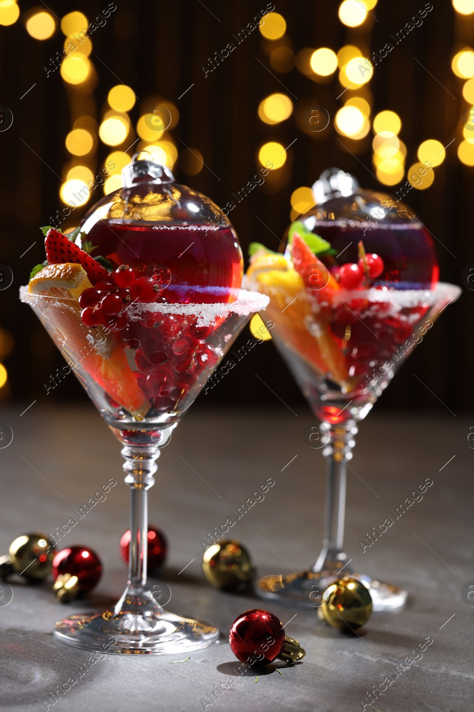 Creative presentation of Christmas Sangria cocktail in baubles and glasses on grey table against black background with blurred lights Photo of Creative presentation of Christmas Sangria cocktail in baubles and glasses on grey table against black background with blurred lights