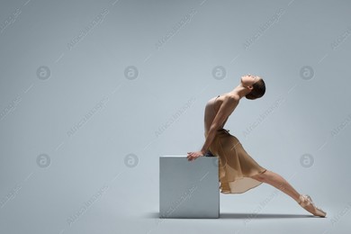 Photo of Young ballerina practicing dance moves on cube against white background. Space for text