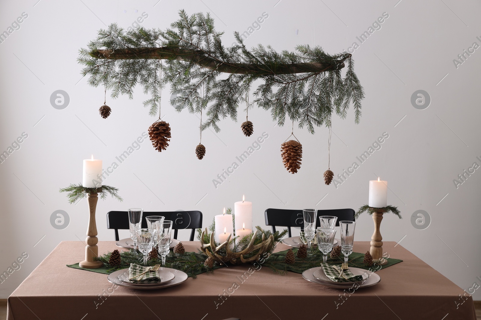Christmas celebration. Cones hanging from fir tree branch over table with burning candles and tableware Photo of Christmas celebration. Cones hanging from fir tree branch over table with burning candles and tableware
