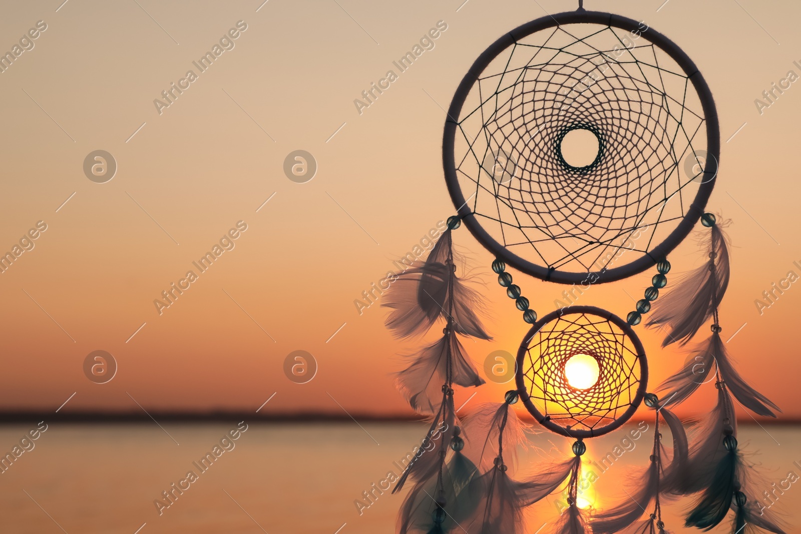 Beautiful handmade dream catcher near river at sunset. Space for text Photo of Beautiful handmade dream catcher near river at sunset. Space for text