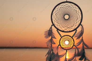 Beautiful handmade dream catcher near river at sunset. Space for text Photo of Beautiful handmade dream catcher near river at sunset. Space for text
