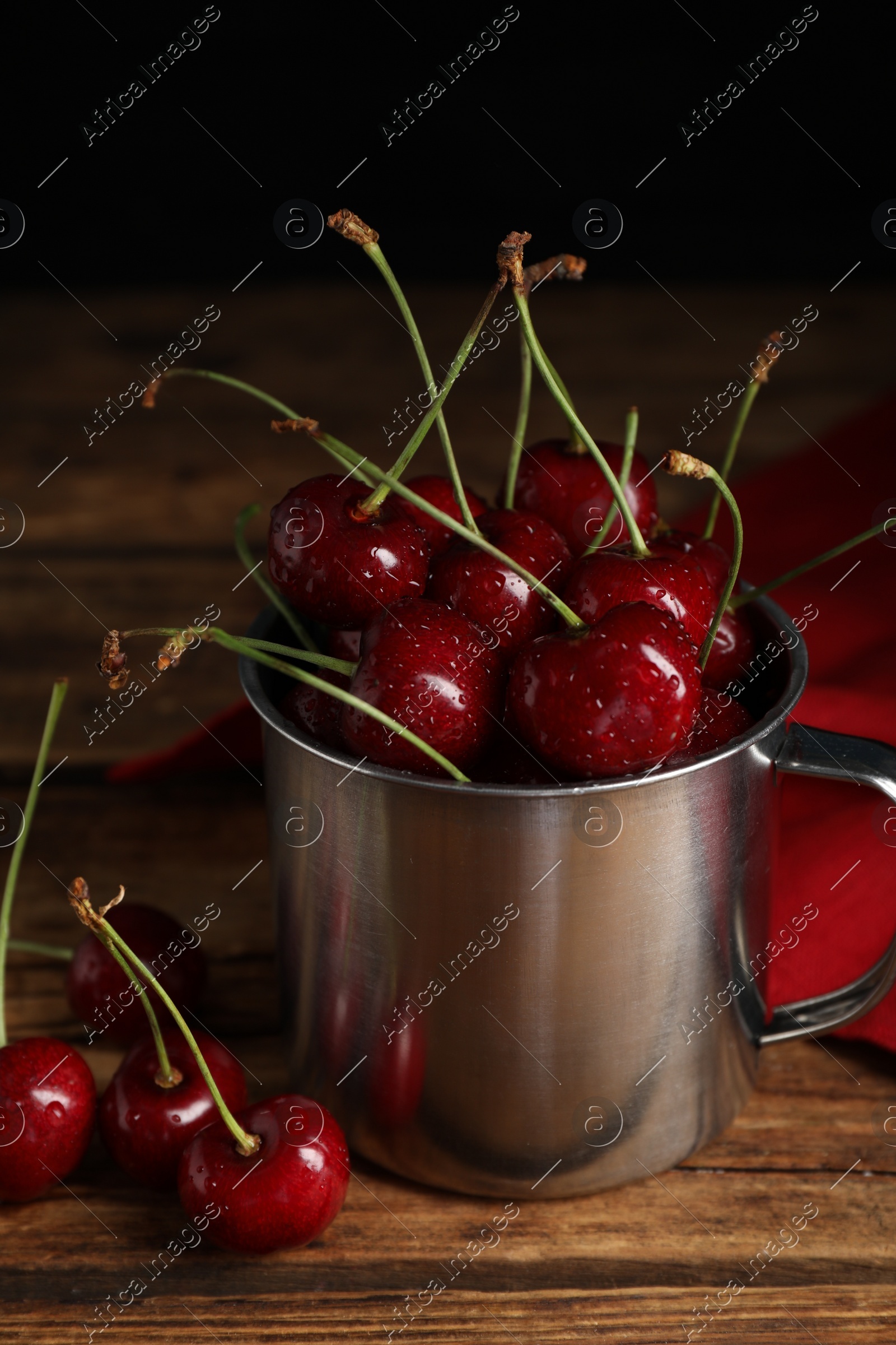 Wet red cherries in enameled mug on wooden table Photo of Wet red cherries in enameled mug on wooden table