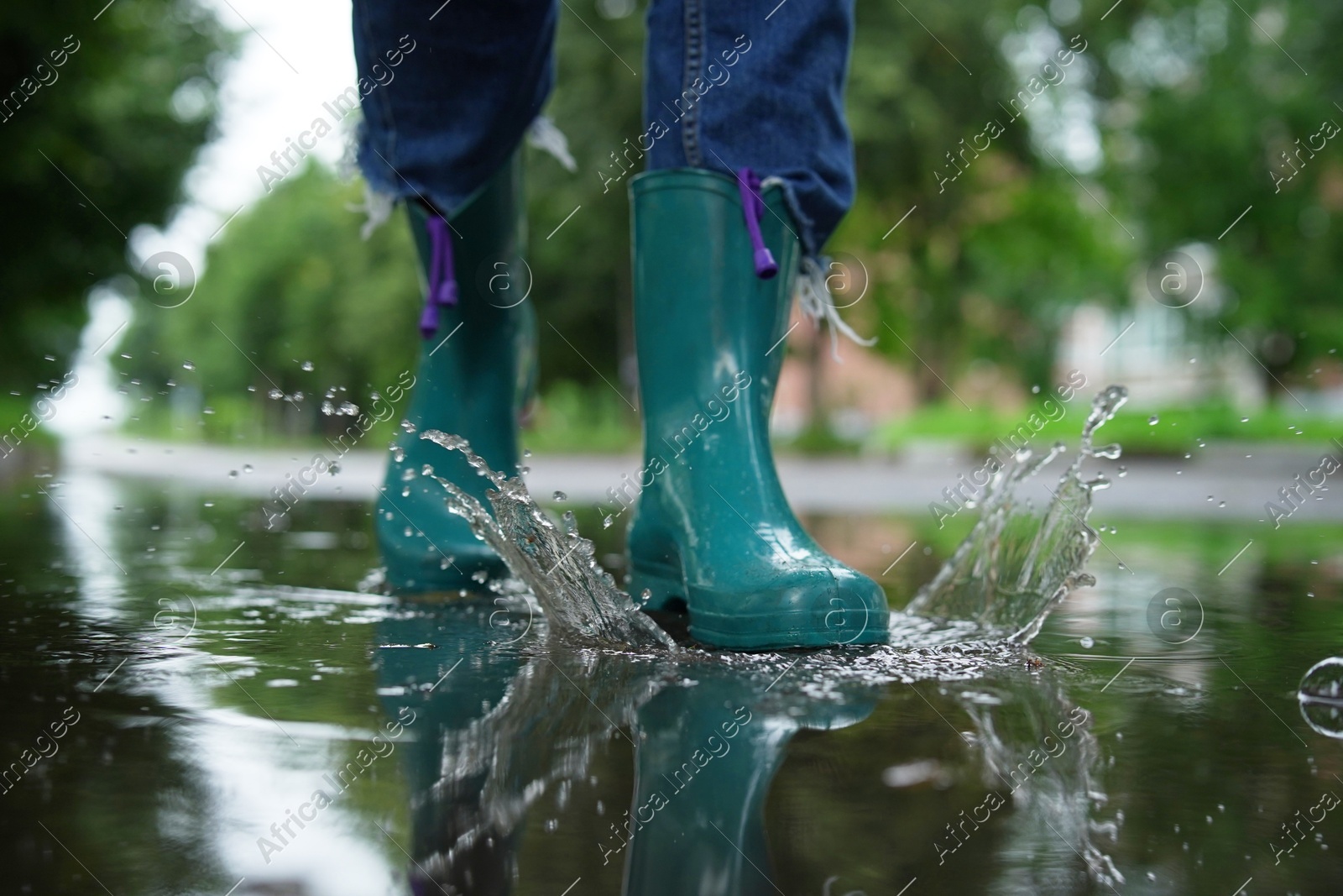 Woman wearing turquoise rubber boots walking in puddle outdoors, closeup Photo of Woman wearing turquoise rubber boots walking in puddle outdoors, closeup