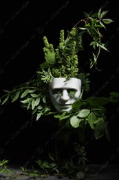 Theatrical performance. Plastic mask and floral decor on table against black background Photo of Theatrical performance. Plastic mask and floral decor on table against black background