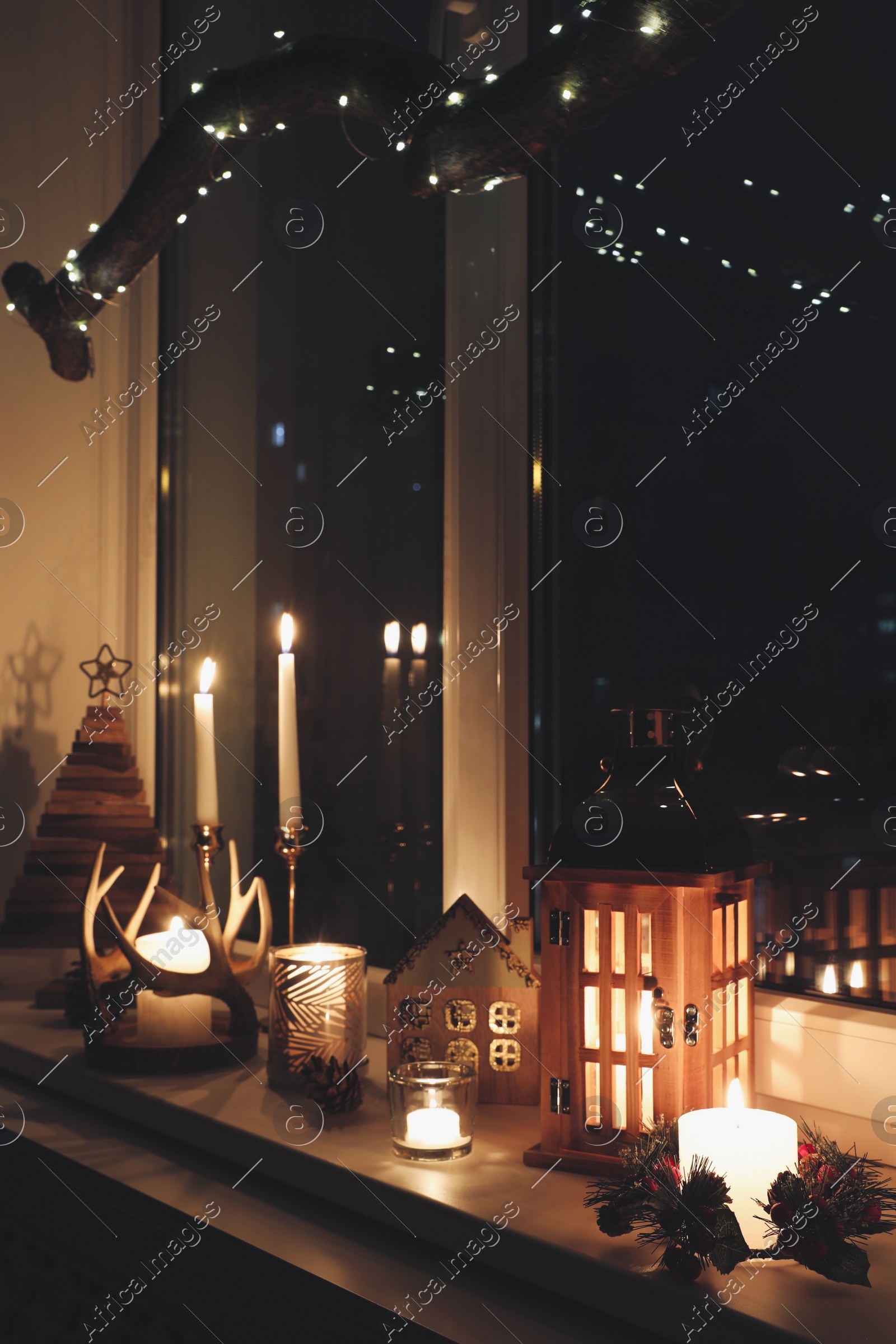 Burning candles and Christmas decor on window sill at night Photo of Burning candles and Christmas decor on window sill at night