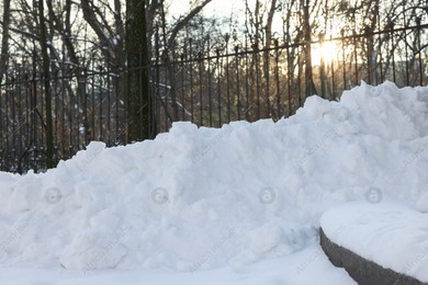Pile of snow, fence and sunbeams shining through trees in winter park Photo of Pile of snow, fence and sunbeams shining through trees in winter park