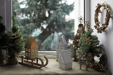 Many beautiful Christmas decorations and small fir trees on window sill indoors Photo of Many beautiful Christmas decorations and small fir trees on window sill indoors