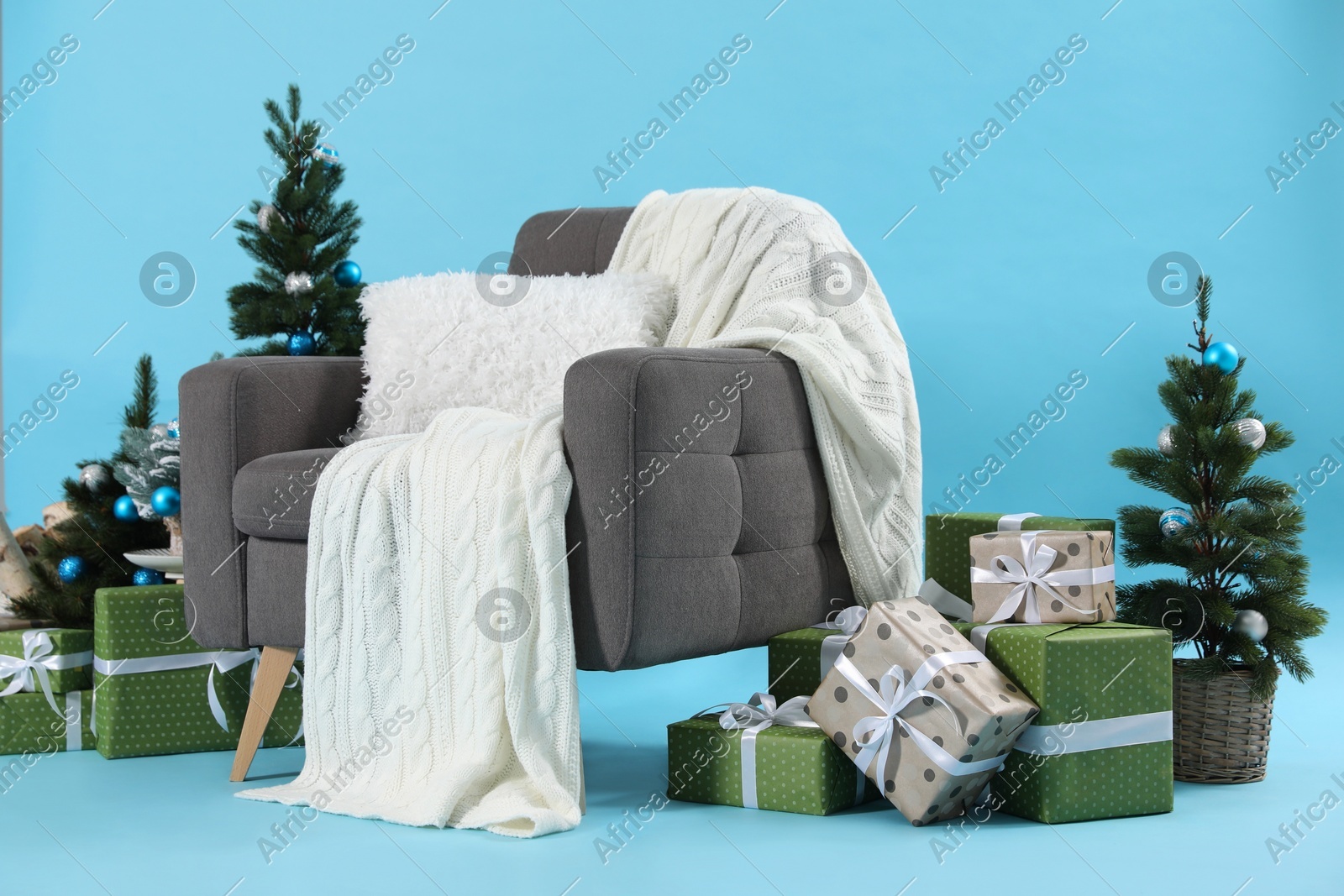 Beautiful Christmas themed photo zone with stylish armchair, trees and gift boxes on light blue background Photo of Beautiful Christmas themed photo zone with stylish armchair, trees and gift boxes on light blue background
