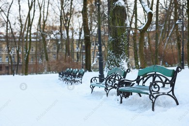 Green benches, trees and buildings in snowy park Photo of Green benches, trees and buildings in snowy park