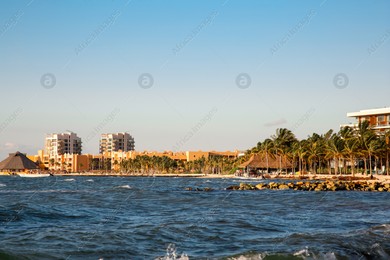 Picturesque view of sea coast, palm trees and distant resort on sunny day Photo of Picturesque view of sea coast, palm trees and distant resort on sunny day