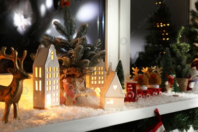 Christmas atmosphere. Beautiful glowing houses, fir trees, artificial snow and toys on window sill indoors Photo of Christmas atmosphere. Beautiful glowing houses, fir trees, artificial snow and toys on window sill indoors