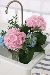 Vase with beautiful hortensia flowers in kitchen sink Photo of Vase with beautiful hortensia flowers in kitchen sink