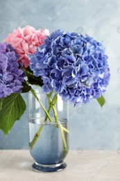 Vase with beautiful hortensia flowers on light table against color background Photo of Vase with beautiful hortensia flowers on light table against color background