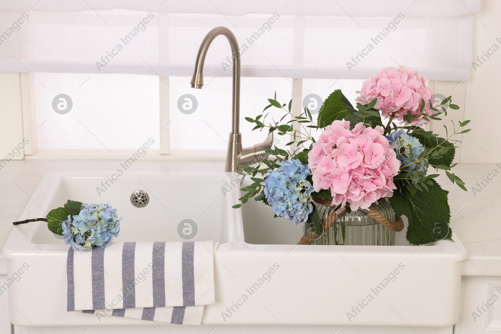 Vase with beautiful hortensia flowers in kitchen sink Photo of Vase with beautiful hortensia flowers in kitchen sink