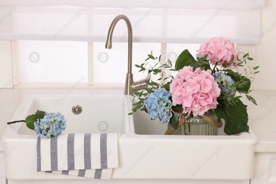 Vase with beautiful hortensia flowers in kitchen sink Photo of Vase with beautiful hortensia flowers in kitchen sink