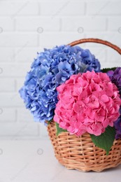 Bouquet with beautiful hortensia flowers in wicker basket on white wooden table near brick wall Photo of Bouquet with beautiful hortensia flowers in wicker basket on white wooden table near brick wall