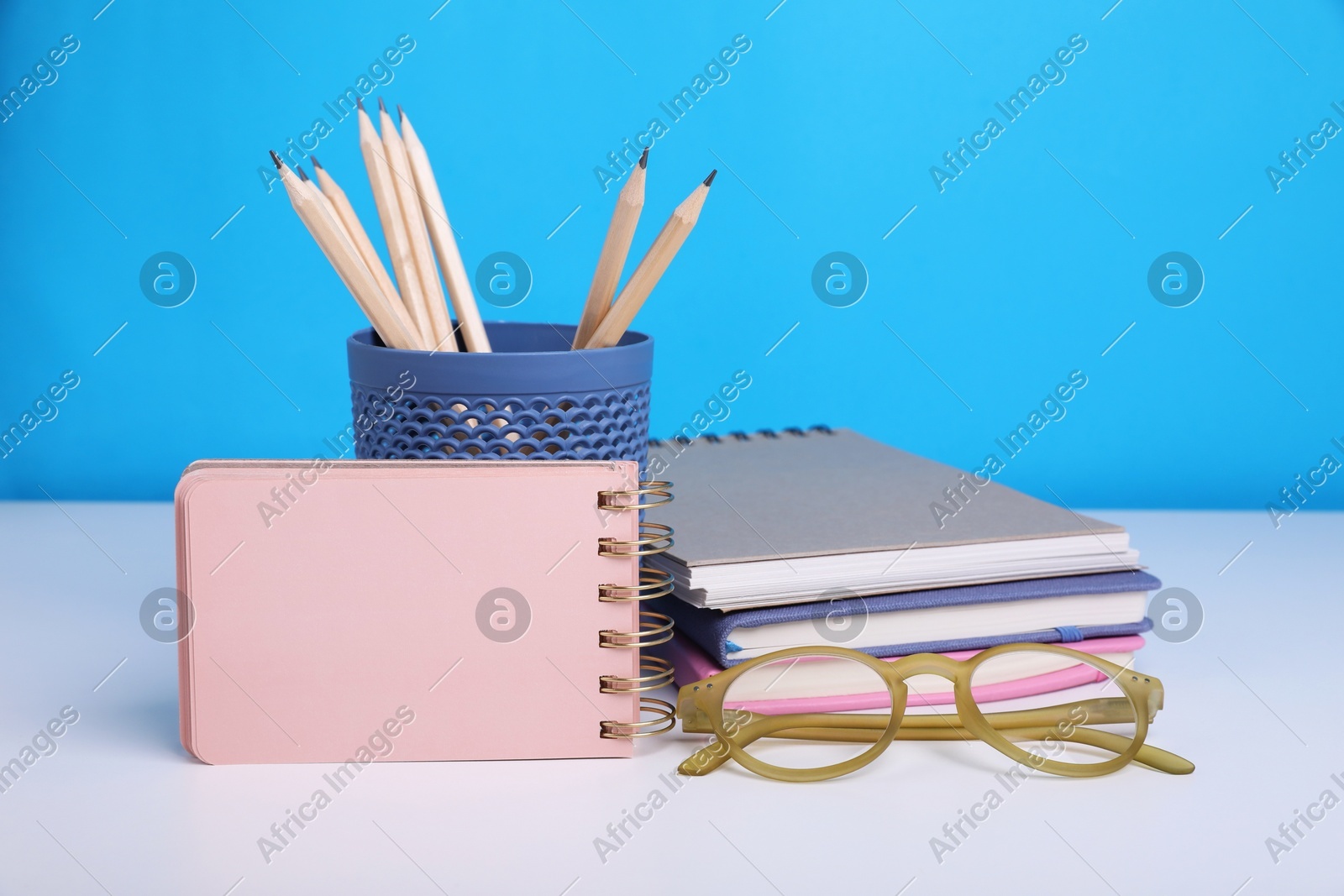 Different school stationery and glasses on white table against light blue background, space for text. Back to school Photo of Different school stationery and glasses on white table against light blue background, space for text. Back to school
