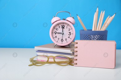 Different school stationery, alarm clock and glasses on white table against light blue background, space for text. Back to school Photo of Different school stationery, alarm clock and glasses on white table against light blue background, space for text. Back to school