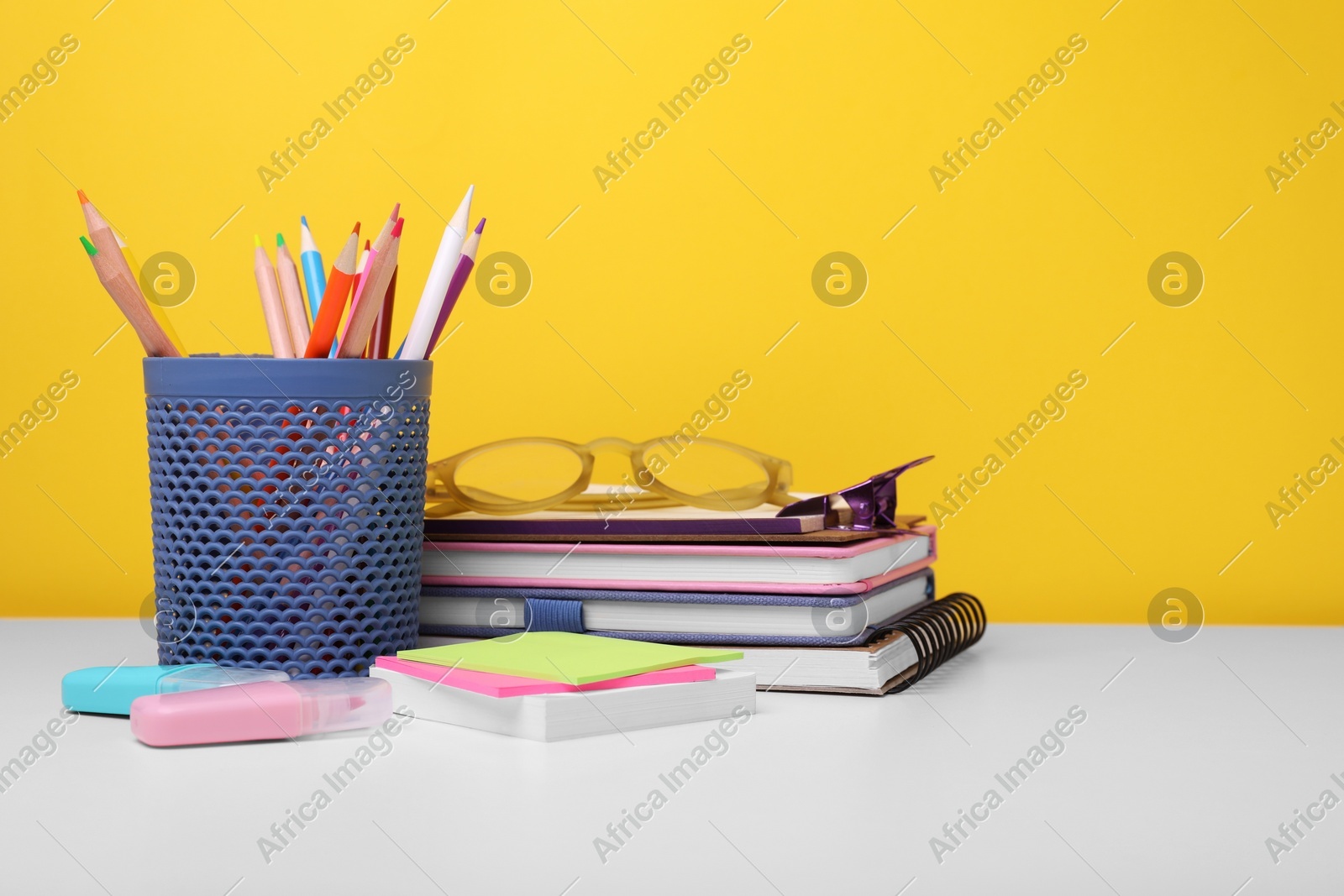 Different school stationery and glasses on white table against yellow background, space for text. Back to school Photo of Different school stationery and glasses on white table against yellow background, space for text. Back to school