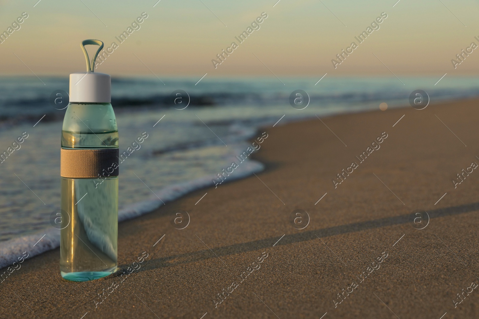Glass bottle with water on wet sand near sea at sunset. Space for text Photo of Glass bottle with water on wet sand near sea at sunset. Space for text